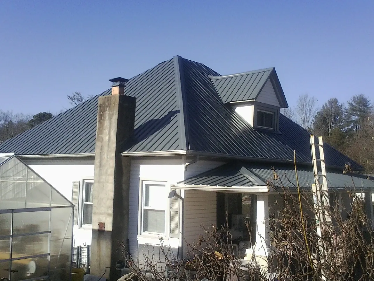 Dark blue standing seam metal roof on a white farmhouse with dormer in Independence
